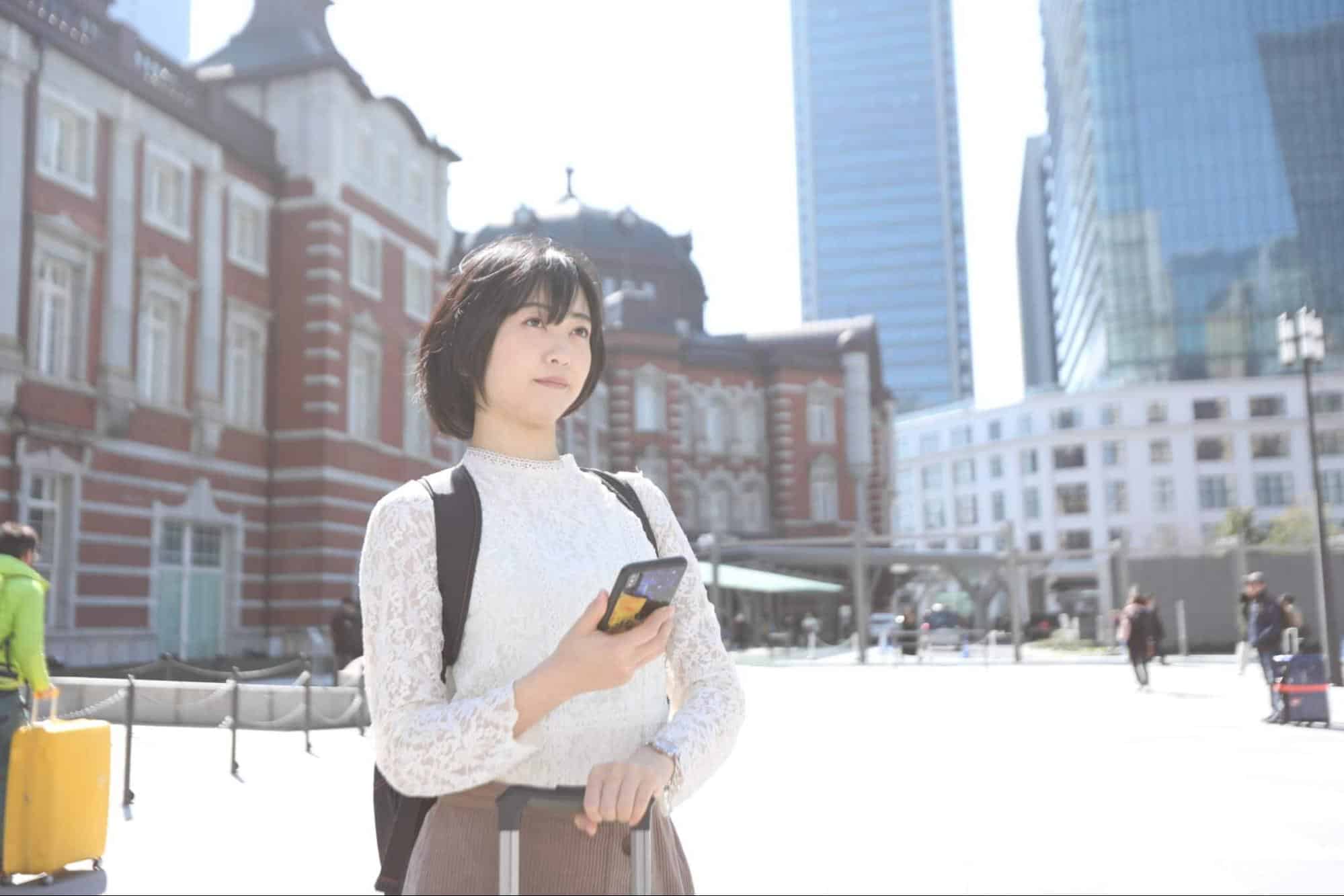 東京駅の前でスマホを持ち遠くを眺める女性