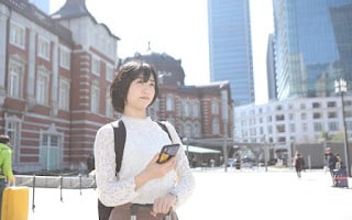 スマホ片手に東京駅でたたずむ女性